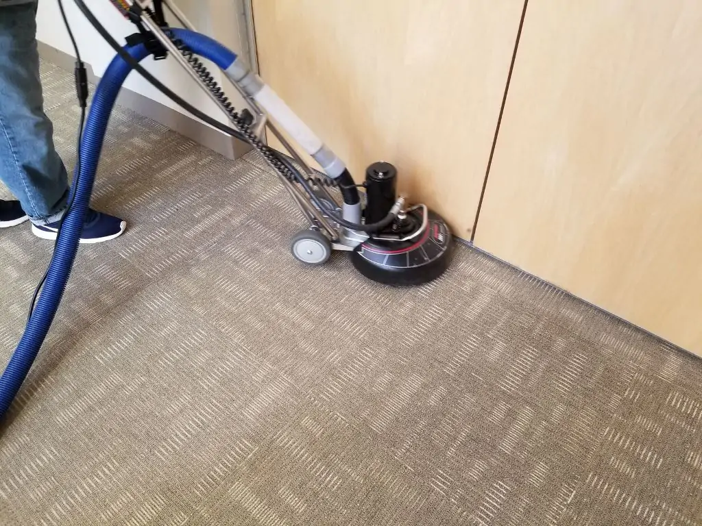 Technician deep cleaning commercial carpet tiles with a rotary extraction machine