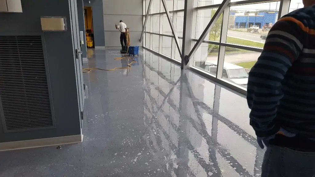Technician using a rotary floor machine to strip a commercial floor covered in stripping solution