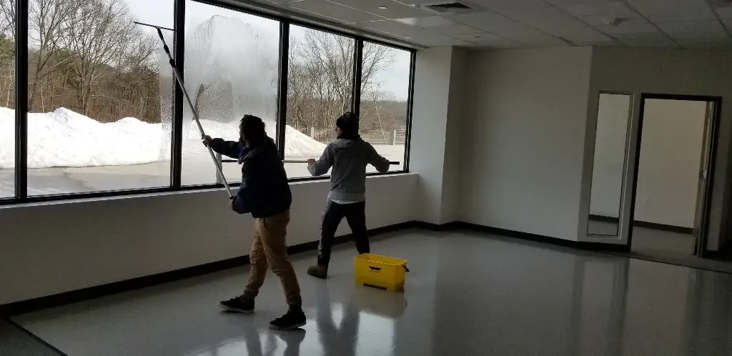 Two crew members squeegeeing soap from office windows inside a commercial building